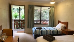 A hotel room with a bed, a desk, and a balcony with a view of greenery. - Green Gables Motel (Warburton)