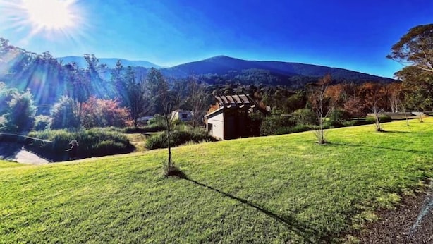 A grassy field with a small building and mountains in the background. - Green Gables Motel (Warburton)