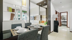 A modern dining area with a glass table, grey upholstered chairs, and a white refrigerator in the background. - Javen by Kozystay - Thamrin (Jakarta)