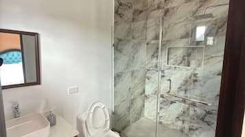 Ein Badezimmer mit einer Marmerdusche, einer weißen Toilette, einem Waschtisch mit Spiegel und einer Holzkabine.