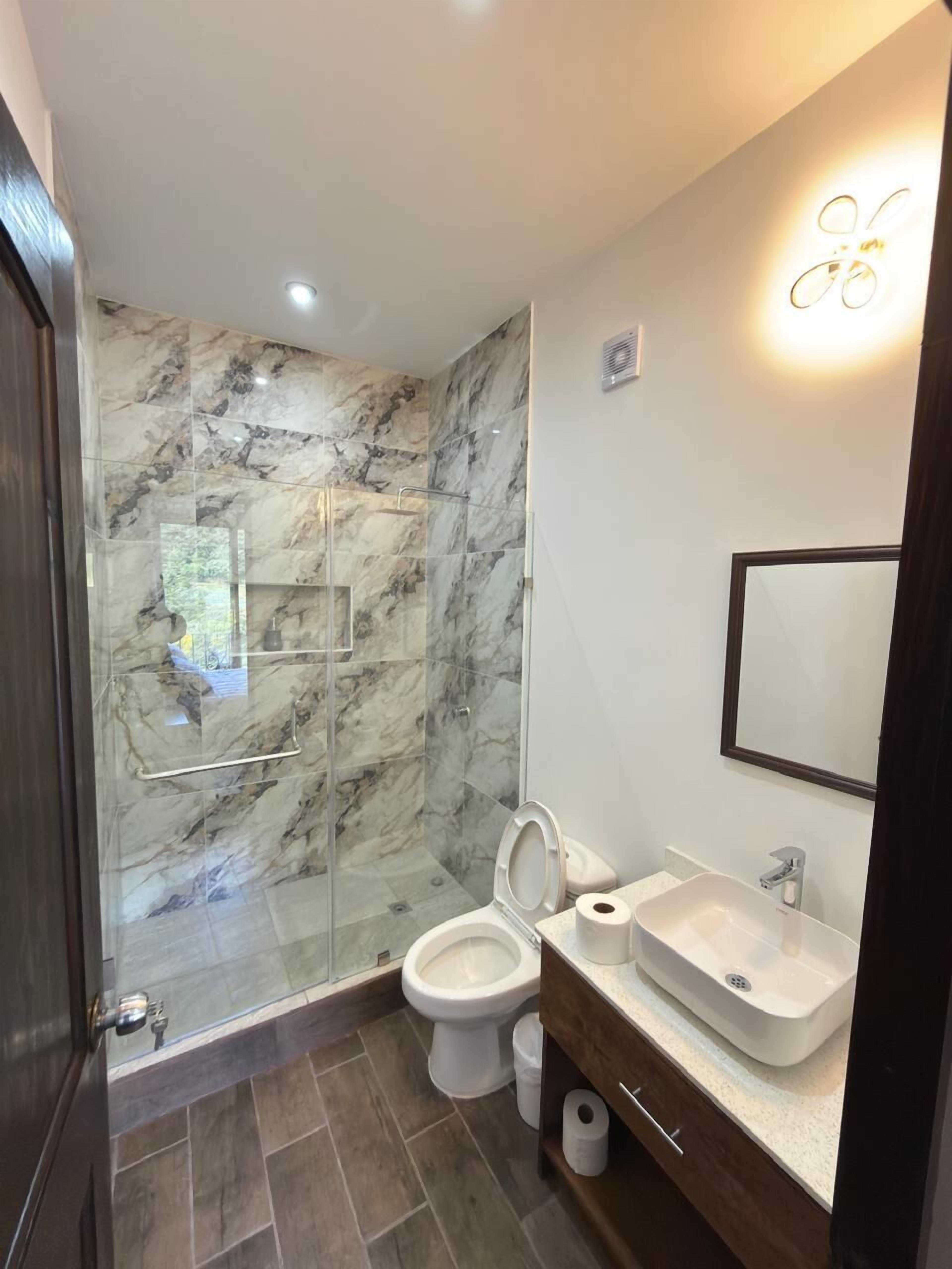 Een moderne badkamer met een douchecabine van glas, een toilet, een wastafel en een spiegel.