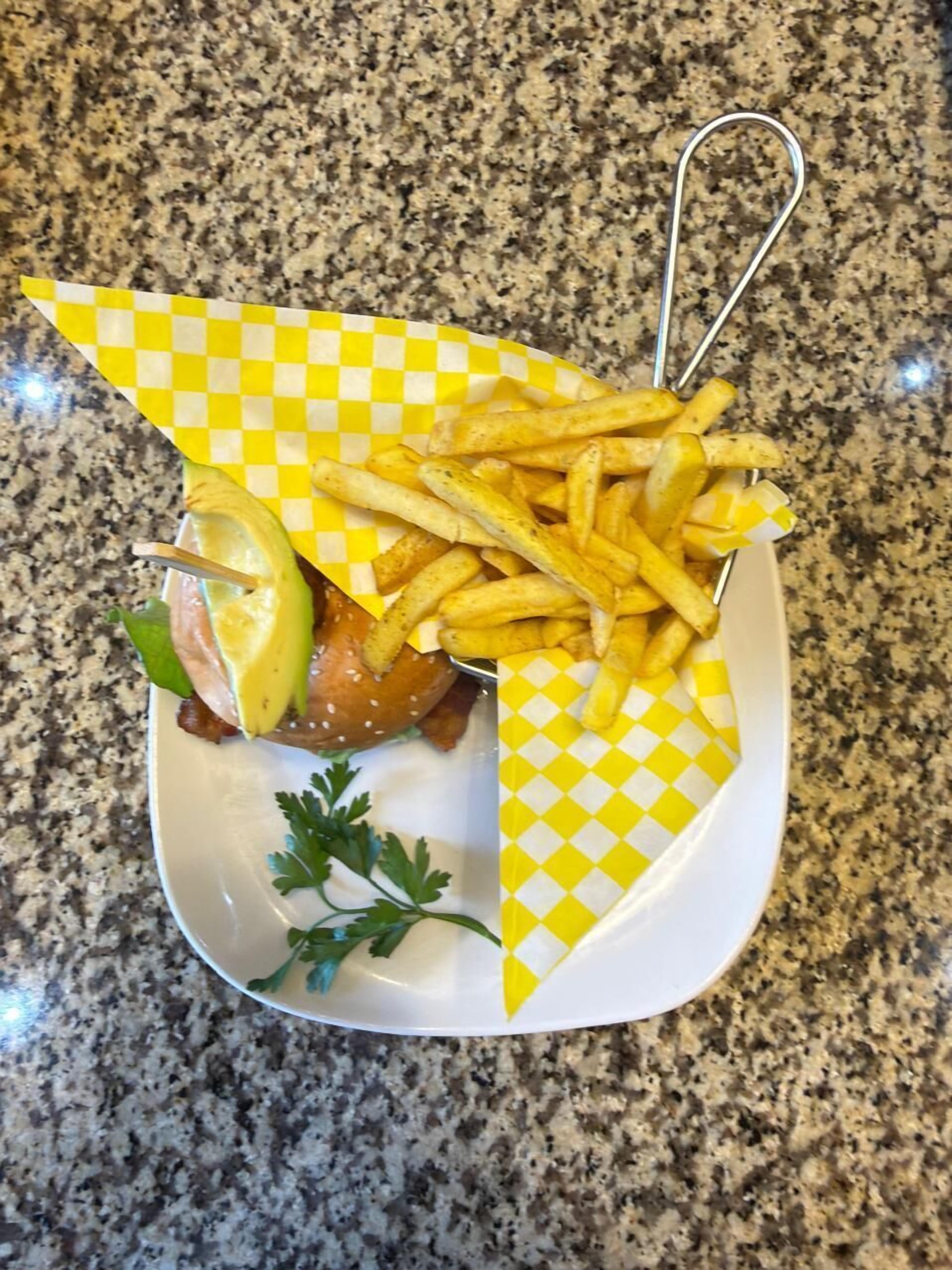 Un plato con un sándwich, papas fritas, una cuña de limón y perejil.
