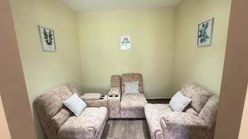 Una habitación pequeña y acogedora con dos sillones beiges y un sillón reclinable central, todos con cojines blancos.