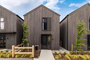 A modern building with a symmetrical facade, a central entrance, and a small garden area with a wooden fence and two young trees.