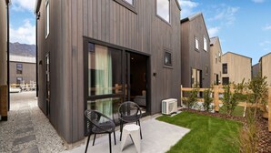A modern house with a large sliding glass door, a small patio with two chairs and a table, and a well-maintained lawn.
