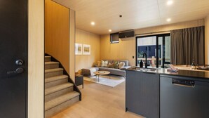 A modern kitchen with a built-in dishwasher, a dining area with a small table and chairs, a sofa, and a staircase leading to another level.