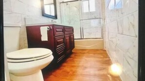 A bathroom with a white toilet, a wooden cabinet, and a bathtub. - SUNNY HOME (Alhambra)