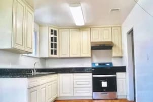 A kitchen with white cabinets, a black countertop, and a stainless steel oven.