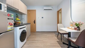 A compact kitchen with a washing machine, a refrigerator, and wooden cabinets. There is a dining area with a table and chairs.