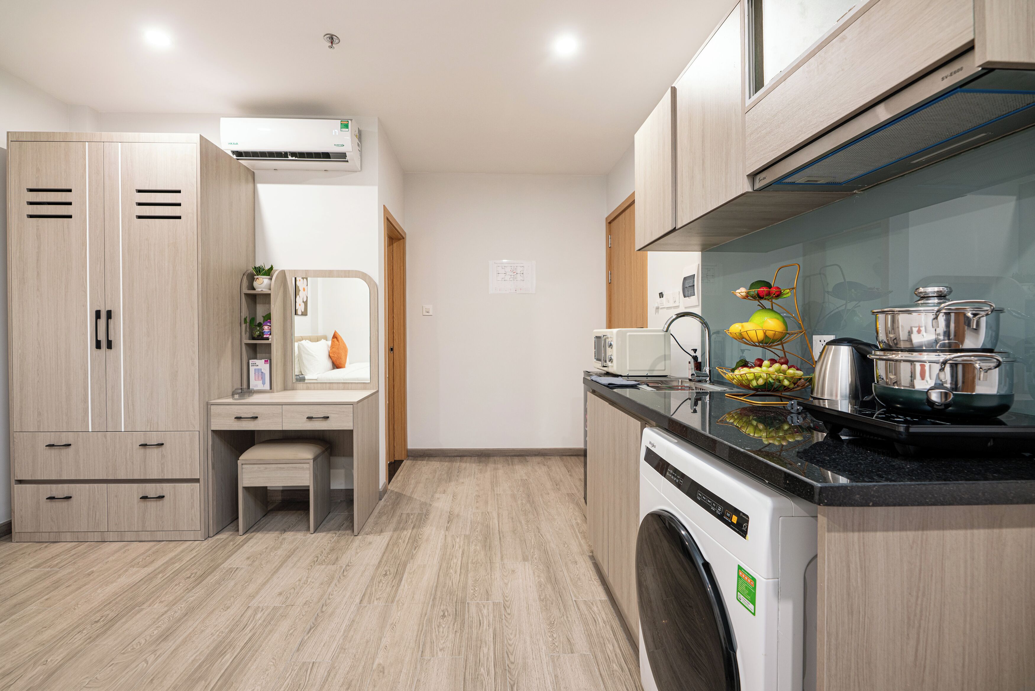 A compact kitchen with a washing machine, a microwave, and a fruit bowl on the counter.