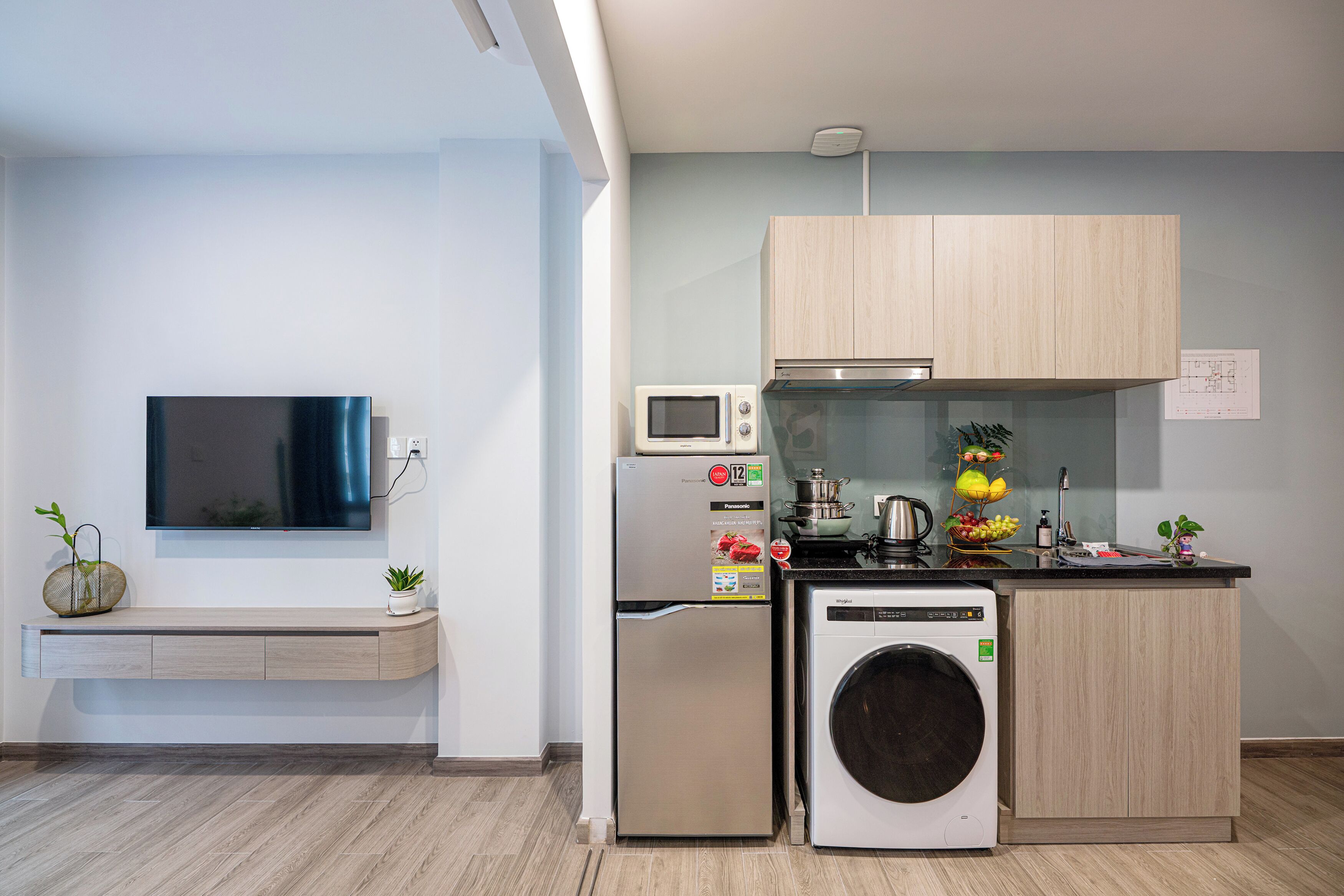 A compact kitchen with a built-in washing machine, a microwave, and a stainless steel refrigerator.
