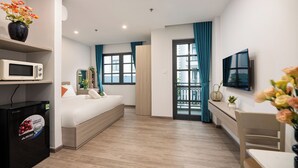 A modern hotel room with a bed, a desk, a TV, a microwave, and a refrigerator.