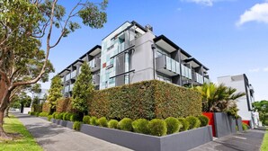 A modern multi-story residential building with a landscaped front garden, a paved walkway, and a clear blue sky. - Modern Abode | Parking & Views near Ponsonby Rd (Auckland Central Suburbs)