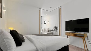 A modern bedroom with a large bed, a TV on a wooden stand, and a view into the bathroom. - Modern Abode | Parking & Views near Ponsonby Rd (Auckland Central Suburbs)
