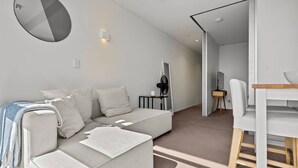 A modern living room with a sectional sofa, a dining table, and a large mirror on the wall. - Modern Abode | Parking & Views near Ponsonby Rd (Auckland Central Suburbs)