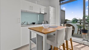 A modern kitchen with white cabinets, a wooden table, and a large window offering a view of the outdoors. - Modern Abode | Parking & Views near Ponsonby Rd (Auckland Central Suburbs)