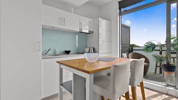 A modern kitchen with white cabinets, a wooden table, and a large window offering a view of the outdoors.