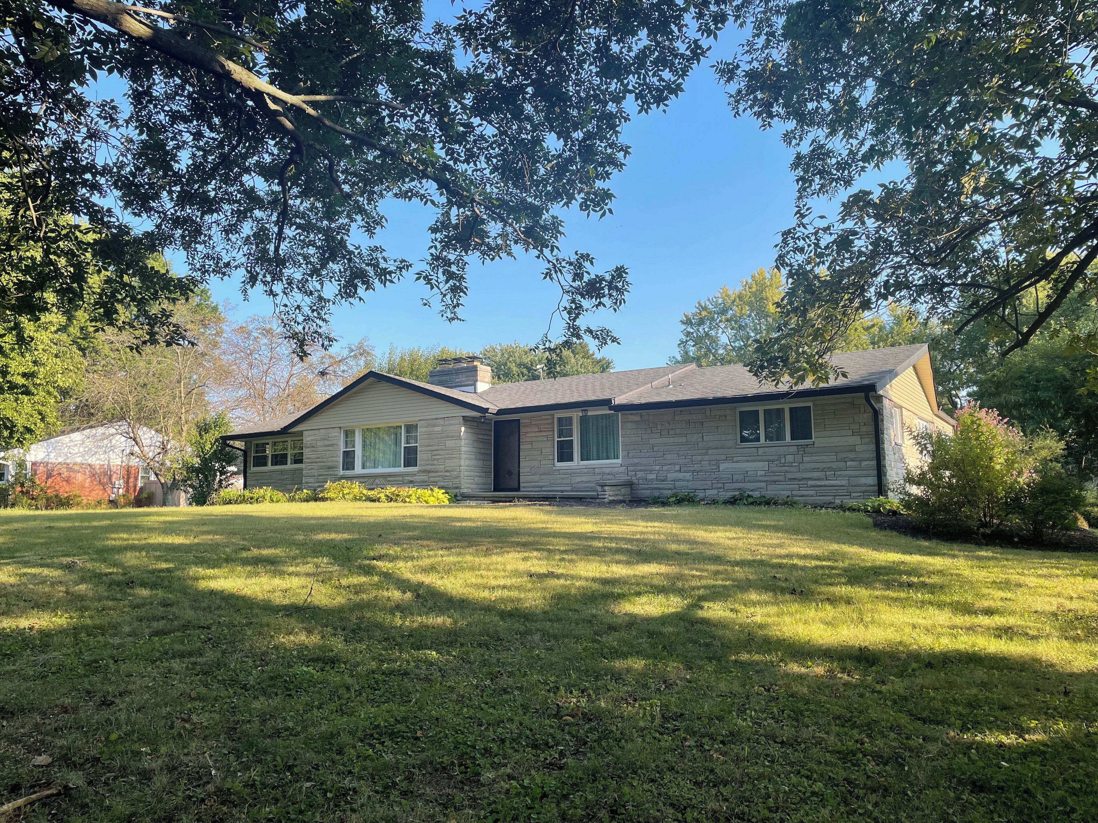 A stone house with a sloped roof, a front porch, and a well-maintained lawn.
