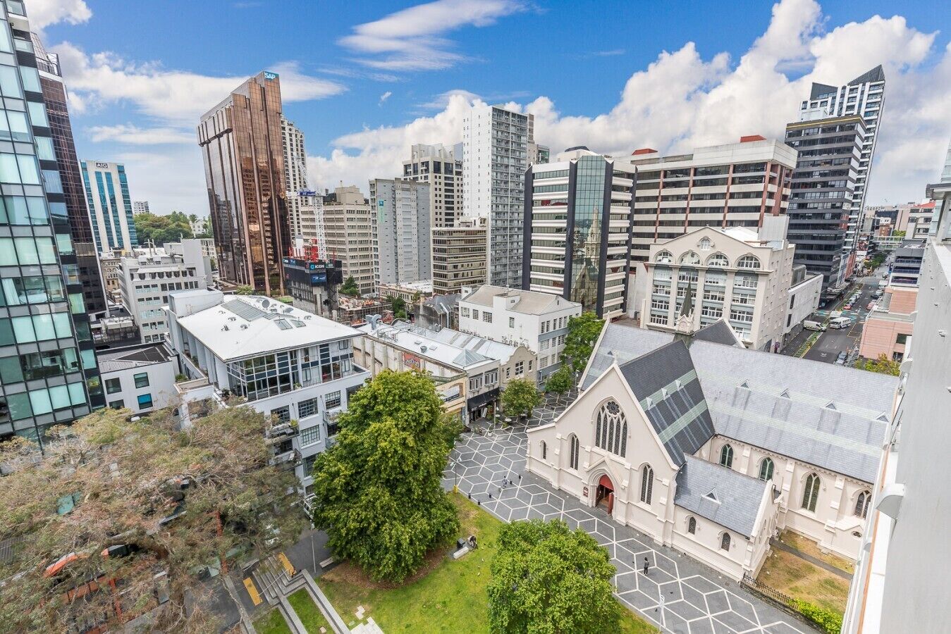 A cityscape with modern buildings, a church, and a green area.