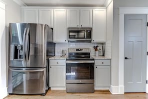 A kitchen with stainless steel appliances, white cabinets, and a tiled backsplash.