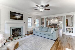 A living room with a fireplace, a sofa, a ceiling fan, and a television.