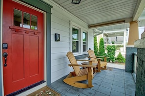 A red door with a mailbox, two Adirondack chairs, and a covered porch with a stone wall.