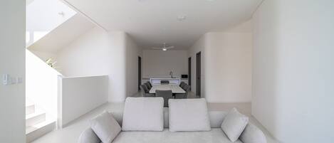 A modern living room with a sofa, a dining table, and two ceiling fans.