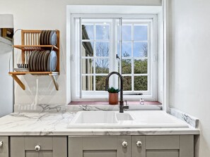 Una cocina con encimera de mármol, un lavamanos y una ventana con vista a árboles.