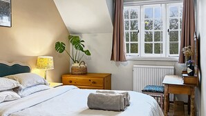Een slaapkamer met een bed, nachtkastje, lamp, een potplant, raam en radiator.