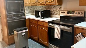 Una cocina con armarios de madera, un microondas, una estufa y un cesto de basura.