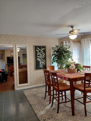 A dining area with a wooden table and chairs, a ceiling fan, and a large potted plant.