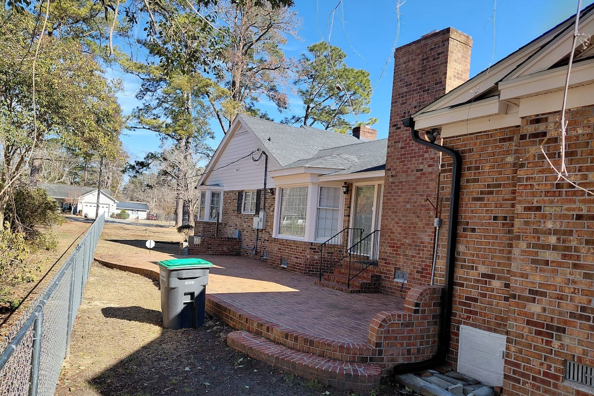 A residential property with a brick exterior, a front porch, and a visible trash bin.