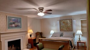 Un dormitorio con cama, una silla, chimenea y ventilador de techo.