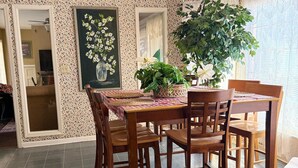 Un área de comedor con una mesa y sillas de madera, un ventilador de techo y un ventanal con cortinas.