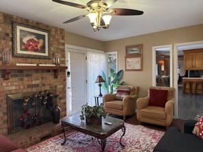 A living room with a fireplace, a ceiling fan, and a dining area visible through an open door. - Large Desirable Corner House (Loris)