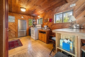 A wooden cabin kitchen with a refrigerator, stove, microwave, and wooden cabinets. - Bear Necessities | Cozy Waterfront Cabin | Lake Views, Pet Friendly, Kayak (Rangeley)