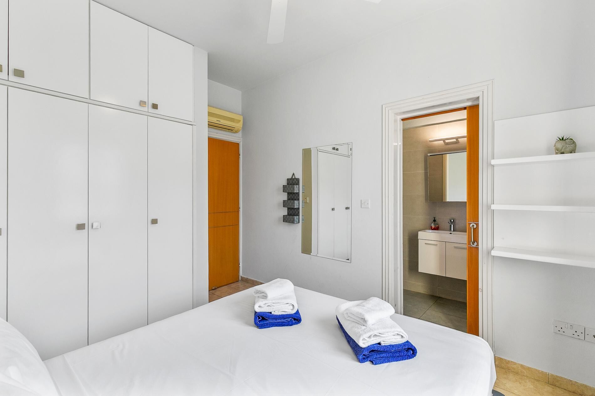 Une chambre d’hôtel avec un lit, une armoire, une salle de bain visible à travers une porte ouverte et une étagère contenant des articles de toilette.