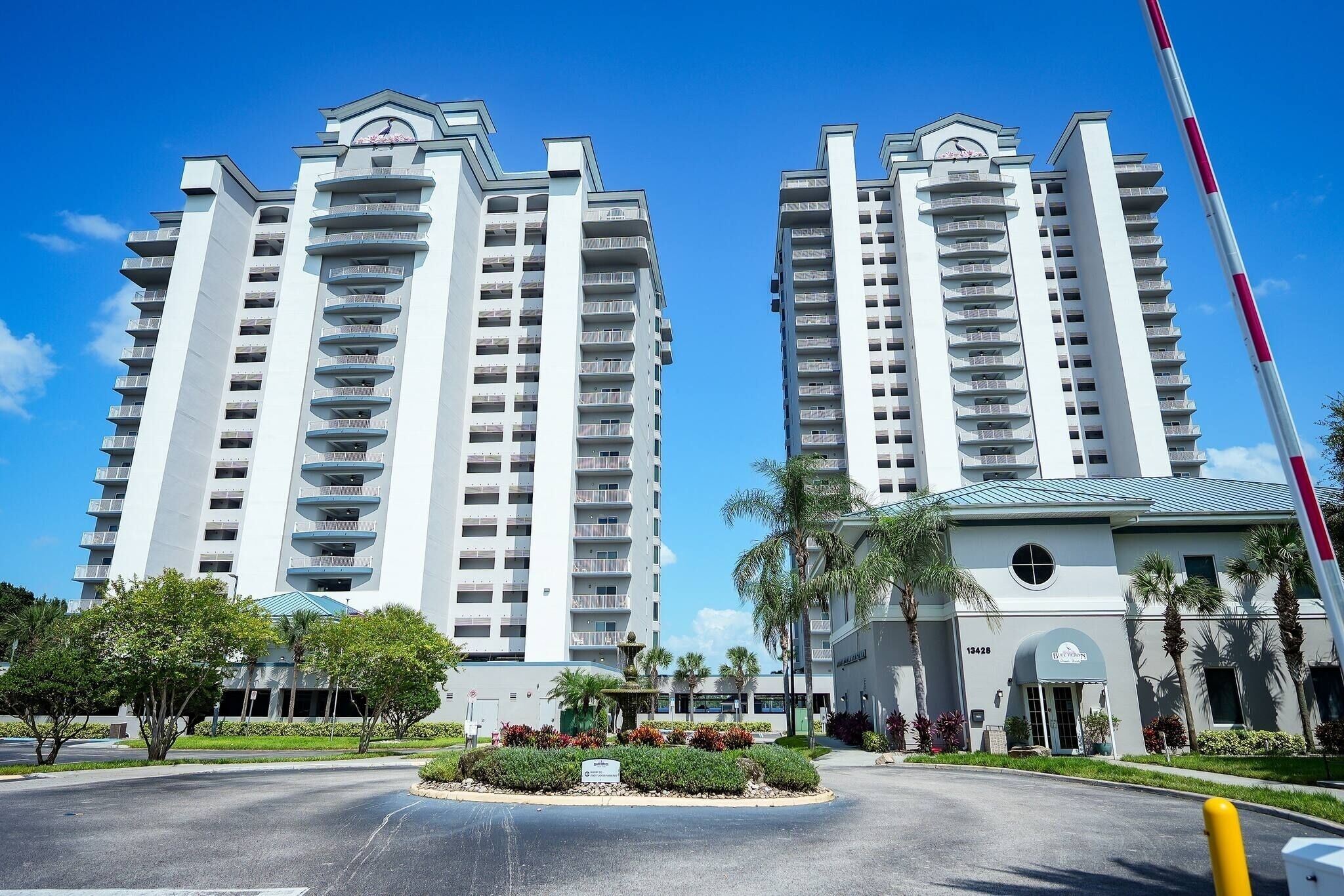 A high-rise hotel with multiple balconies, a central courtyard with palm trees, and a clear blue sky.
