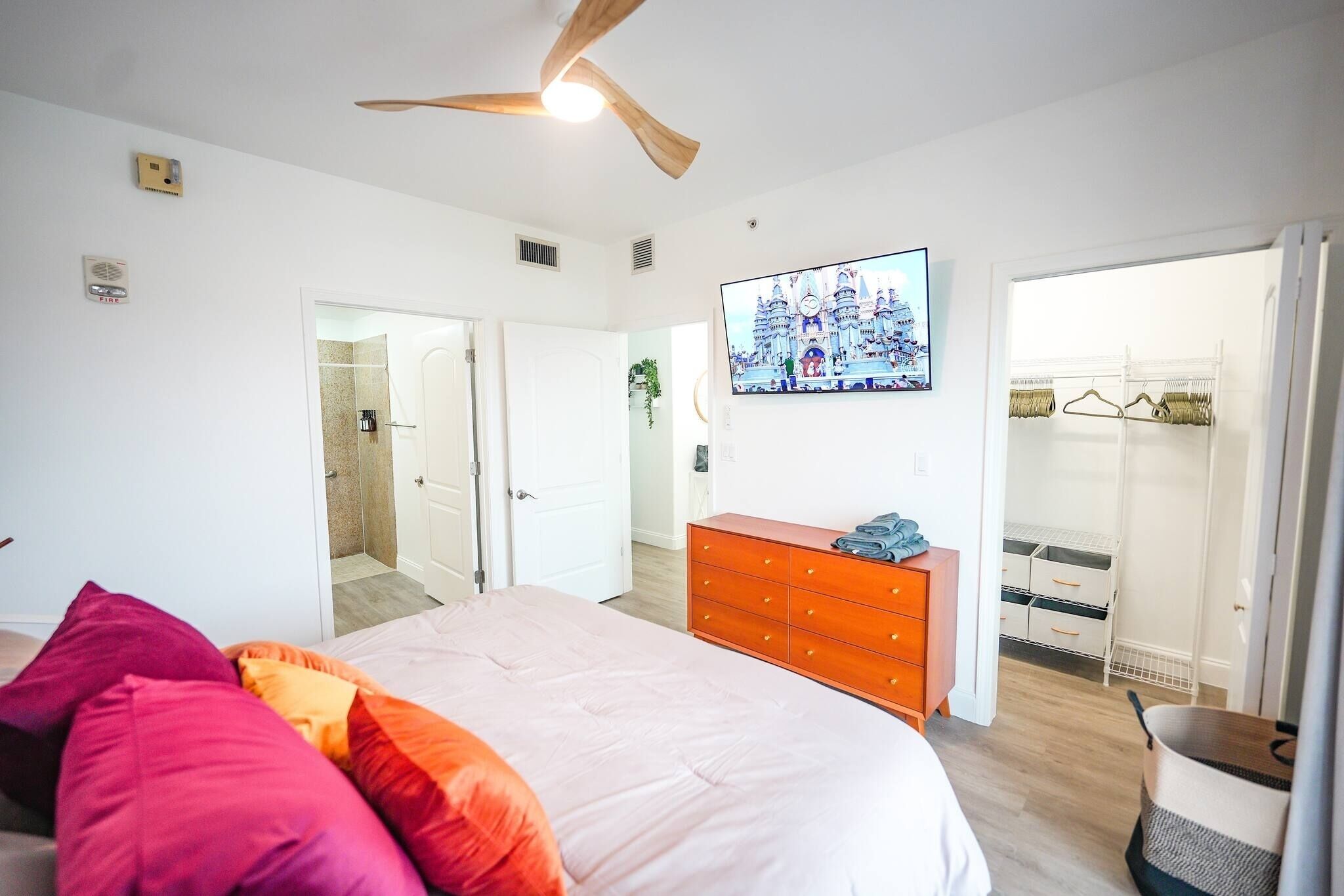 Ein Schlafzimmer mit Bett, Kommode, Deckenventilator, Fernseher und Kleiderschrank.