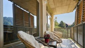 Un balcón con sillas de mimbre y una mesita, ventanas amplias y vistas al exterior.