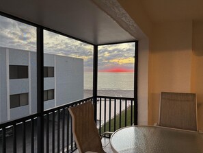 A balcony with a view of the ocean during sunset, a glass table, and two chairs. - La Coquina Gulf-Front – Beach, Pool & Sunset Views (Englewood)