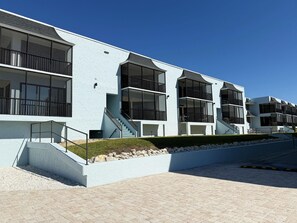 A modern building with multiple balconies and large windows, featuring a light blue exterior and a paved walkway. - La Coquina Gulf-Front – Beach, Pool & Sunset Views (Englewood)