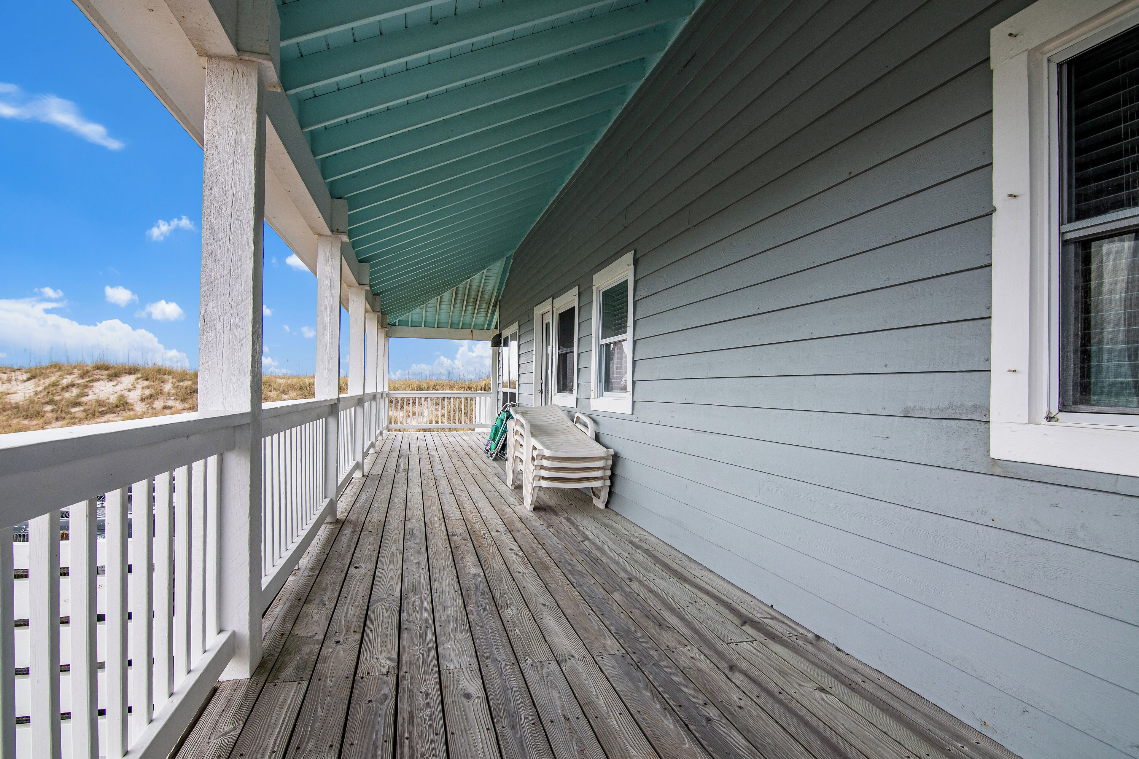 Une terrasse en bois avec une balustrade blanche, un toit végétalisé et une vue sur la plage.