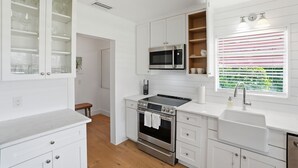 Une cuisine moderne avec des meubles blancs, un four à micro-ondes encastré, un four en acier inoxydable et une fenêtre avec des stores à rayures.