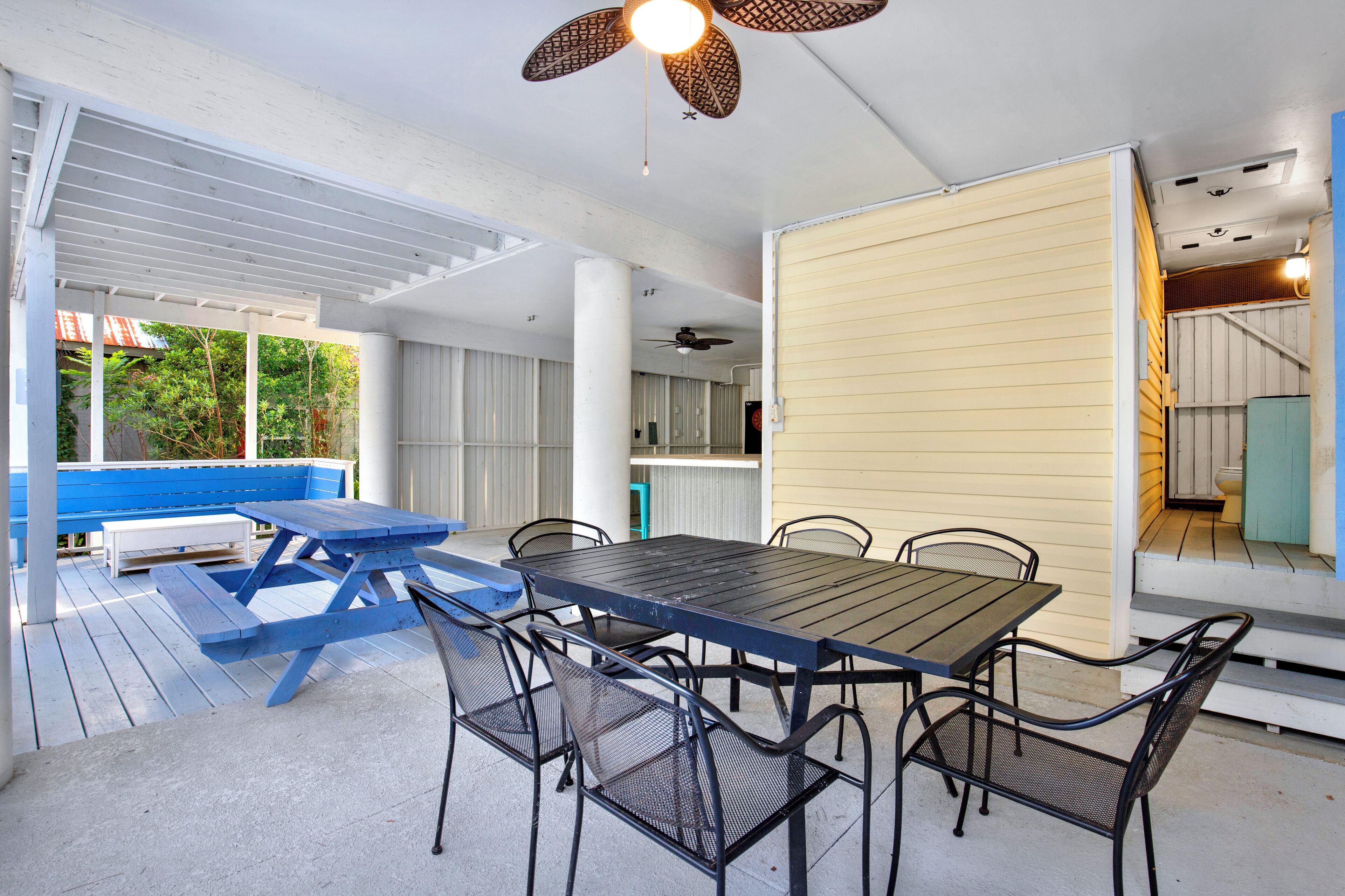 Um pátio externo com mesa e cadeiras de piquenique, um banco azul e um ventilador de teto.
