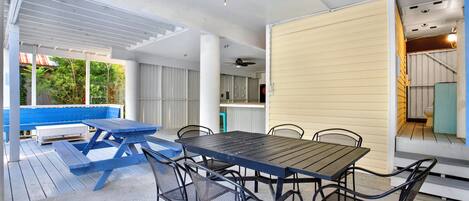 Um pátio externo com mesa e cadeiras de piquenique, um banco azul e um ventilador de teto.