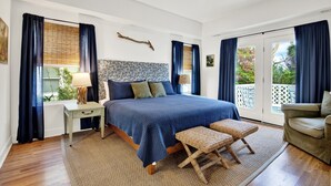 Ein Schlafzimmer mit einem großen Bett, einem Nachttisch, einer Lampe, einem Sessel und Blick ins Freie.