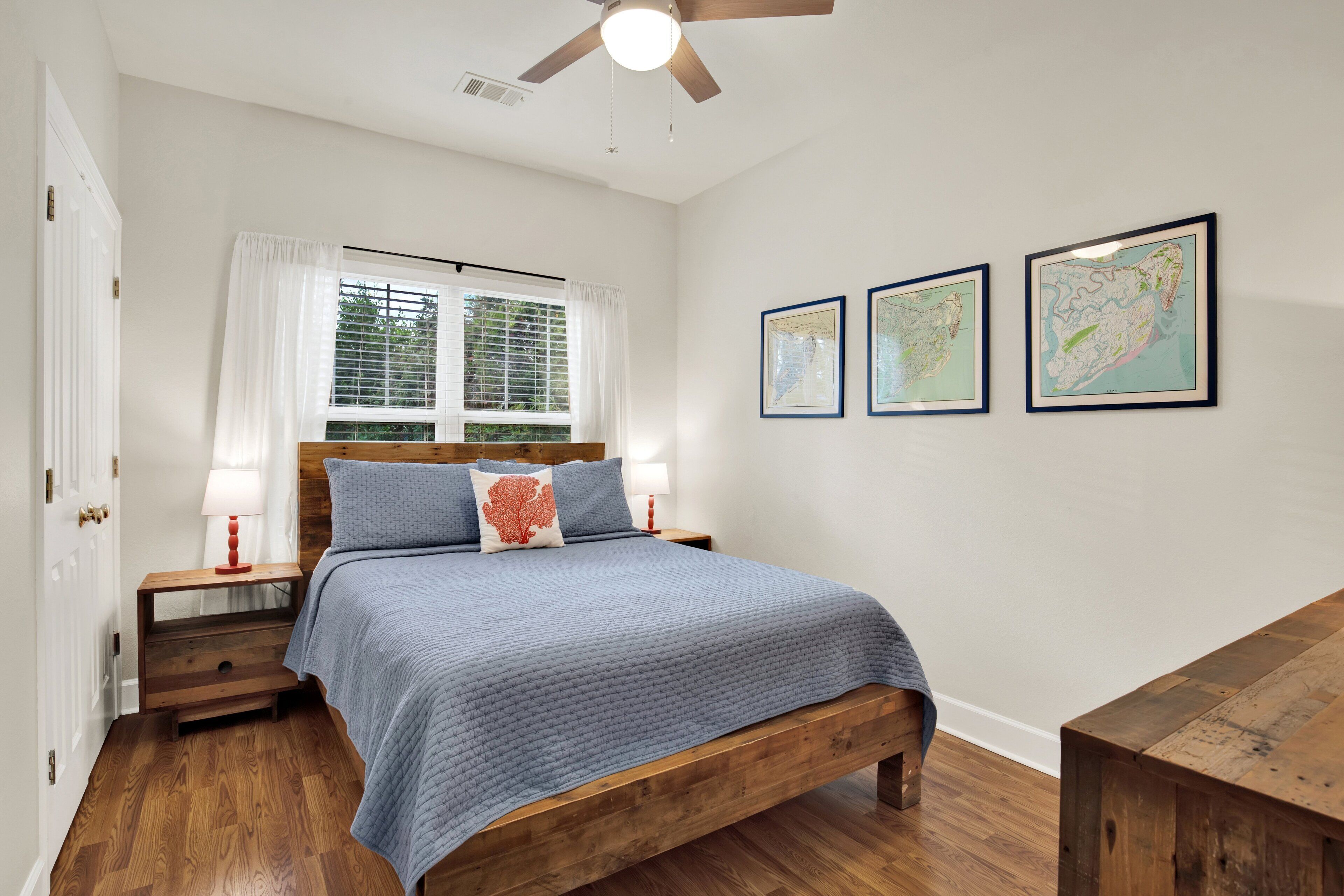 A bedroom with a wooden bed, white walls, a ceiling fan, and two framed maps on the wall.