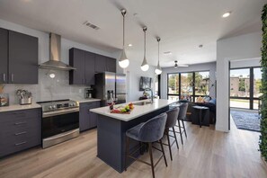 Una cocina moderna con una isla central, electrodomésticos de acero inoxidable e iluminación colgante.