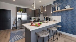 Une cuisine moderne avec un îlot central, des tabourets de bar et un mur orné d’un motif bleu.